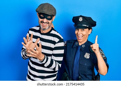 Middle Age Couple Of Hispanic Woman And Man Wearing Thief And Police Uniform With A Big Smile On Face, Pointing With Hand Finger To The Side Looking At The Camera. 