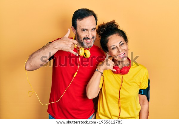 Middle age\
couple of hispanic woman and man wearing sportswear and arm band\
smiling doing phone gesture with hand and fingers like talking on\
the telephone. communicating concepts.\
