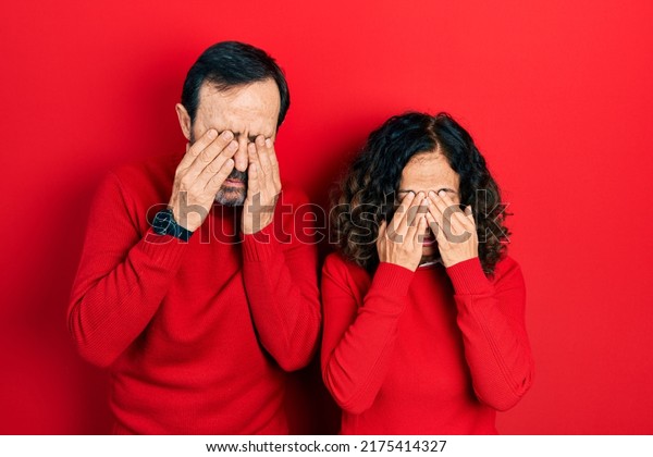 Middle age couple of hispanic woman and\
man hugging and standing together rubbing eyes for fatigue and\
headache, sleepy and tired expression. vision problem\
