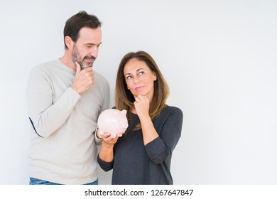 Middle Age Couple Holding Piggy Bank Over Isolated Background Serious Face Thinking About Question, Very Confused Idea