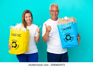 Middle Age Couple Holding A Recycling Bags Full Of Paper And Plastic Isolated On White Background Giving A Thumbs Up Gesture With Both Hands And Smiling