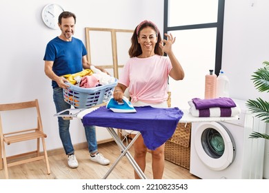 Middle Age Couple Ironing Clothes At Home Doing Ok Sign With Fingers, Smiling Friendly Gesturing Excellent Symbol 