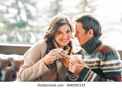 Middle Age Couple Resting On Leather Couch, Drinking Coffee, Wearing Warm Cozy Pullovers