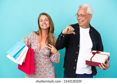 Middle Age Couple With Shopping Bag And Gift Isolated On Blue Background Proud And Self-satisfied In Love Yourself Concept