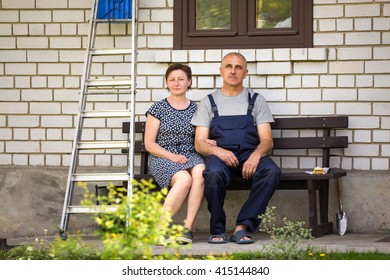 Middle Age Couple Sitting On The Bench Near Country House