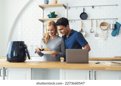 Middle age couple smiling and hugging each other cooking toast bread healthy with recipe by Air Fryer machine,using laptop computer while ecommerce shopping online in grocery store in kitchen at home. - Powered by Shutterstock