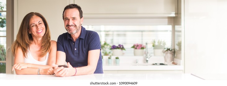 Middle Age Couple, Woman And Man Using Smartphone At Kitchen. Ultra Wide Home Shot.