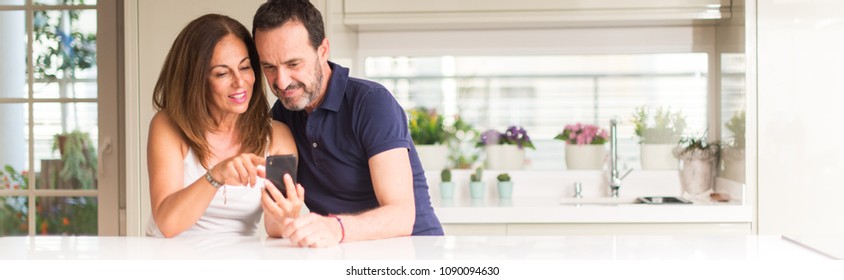 Middle Age Couple, Woman And Man Using Smartphone At Kitchen. Ultra Wide Home Shot.