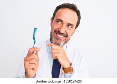 Middle age dentist man holding toothbrush standing over isolated white background serious face thinking about question, very confused idea