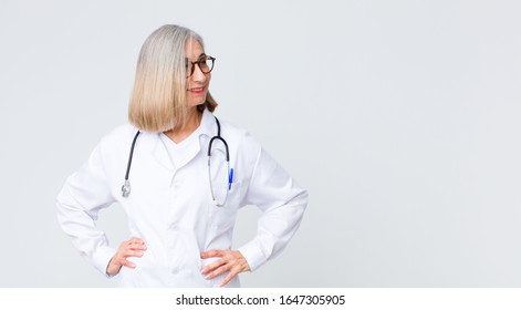 Middle Age Doctor Woman Looking Happy, Cheerful And Confident, Smiling Proudly And Looking To Side With Both Hands On Hips