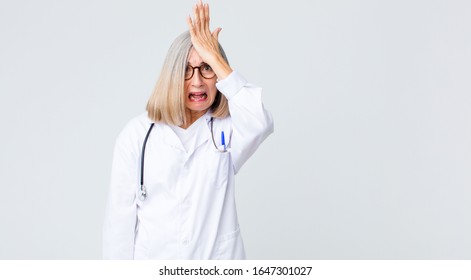 Middle Age Doctor Woman Raising Palm To Forehead Thinking Oops, After Making A Stupid Mistake Or Remembering, Feeling Dumb