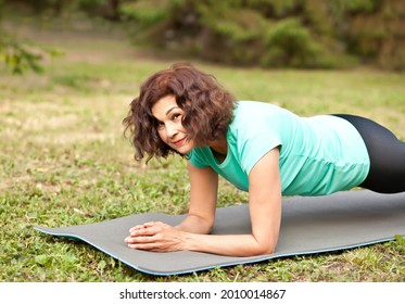 Middle age elderly woman doing plank on yoga mat in a park outdoor - Powered by Shutterstock