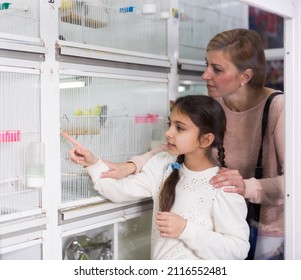 Middle Age European Woman With Kid Girl Visiting Pet Shop And Looking For Bird