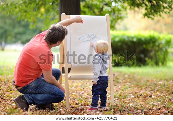 Middle age\
father and his toddler son drawing\
car\

