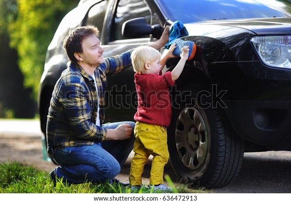 Middle age father with his\
toddler son washing car together outdoors. Family together\
activity