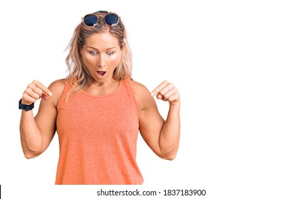 Middle age fit blonde woman wearing casual summer clothes and sunglasses pointing down with fingers showing advertisement, surprised face and open mouth 