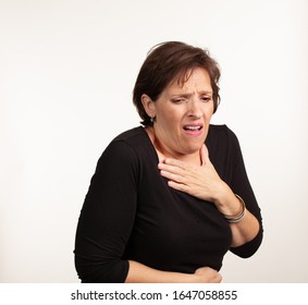 Middle Age Gen X Caucasian Woman In Black On A White Background Making A Painful Or Upset Expresison. Unwell Painful Concept.