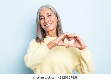 middle age gray hair woman smiling and feeling happy, cute, romantic and in love, making heart shape with both hands - Powered by Shutterstock