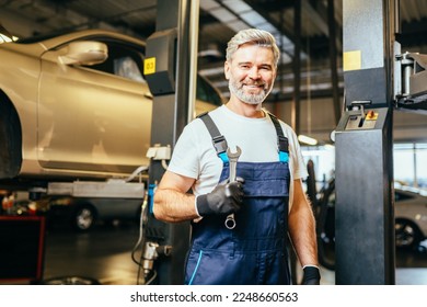 Middle age grey haired mechanic man or smith repairing car at workshop. Professional Mechanic with wrench in garage. - Powered by Shutterstock