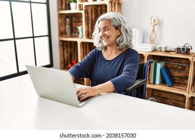 Middle age grey-haired disabled woman using laptop sitting on wheelchair at home. - Powered by Shutterstock