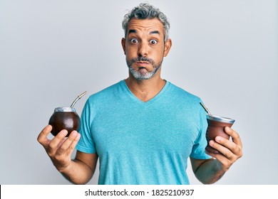 Middle age grey-haired man drinking mate infusion puffing cheeks with funny face. mouth inflated with air, catching air. 