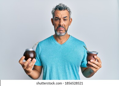 Middle age grey-haired man drinking mate infusion depressed and worry for distress, crying angry and afraid. sad expression. 