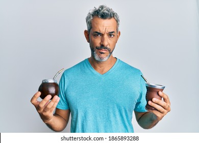 Middle age grey-haired man drinking mate infusion skeptic and nervous, frowning upset because of problem. negative person. 