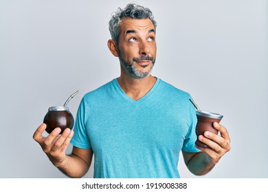 Middle age grey-haired man drinking mate infusion smiling looking to the side and staring away thinking. 