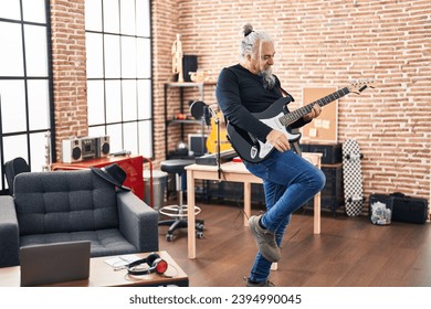 Middle age grey-haired man musician playing electrical guitar dancing at music studio - Powered by Shutterstock