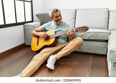 Middle Age Grey-haired Man Playing Classical Guitar Sitting On Floor At Home