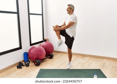 Middle age grey-haired man smiling confident stretching leg at sport center - Powered by Shutterstock