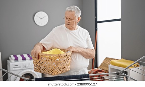 Middle age grey-haired man smiling confident holding basket with clothes at laundry room - Powered by Shutterstock