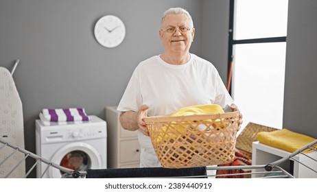 Middle age grey-haired man smiling confident holding basket with clothes at laundry room - Powered by Shutterstock