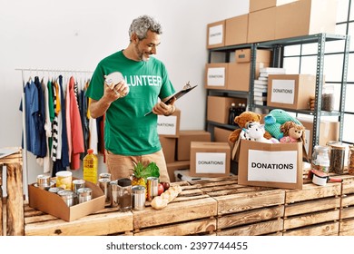 Middle age grey-haired man volunteer reading document holding canned food at charity center - Powered by Shutterstock