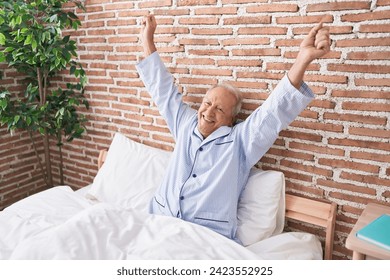 Middle age grey-haired man waking up stretching arms at bedroom - Powered by Shutterstock