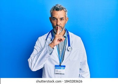 Middle age grey-haired man wearing doctor uniform and stethoscope asking to be quiet with finger on lips. silence and secret concept. 