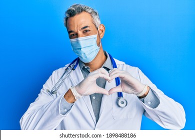 Middle Age Grey-haired Man Wearing Doctor Uniform And Medical Mask Smiling In Love Doing Heart Symbol Shape With Hands. Romantic Concept. 