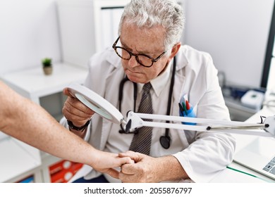 Middle Age Grey-haired Man Wearing Dermatologist Uniform Examining Skin Arm Using Loupe At Dermatology Clinic