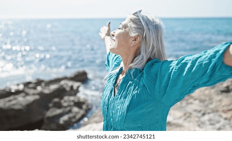 Middle age grey-haired woman breathing with arms open at seaside - Powered by Shutterstock