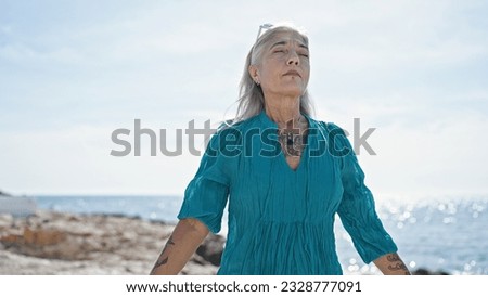 Middle age grey-haired woman breathing with arms open at beach