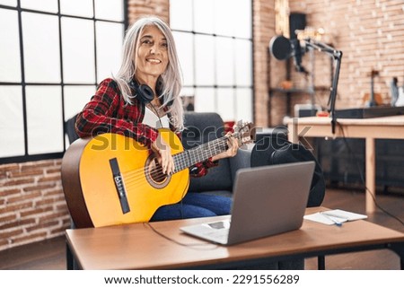 Middle age grey-haired woman musician playing classical guitar at music studio