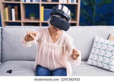 Middle age grey-haired woman playing motorbike video game using virtual reality glasses at home - Powered by Shutterstock