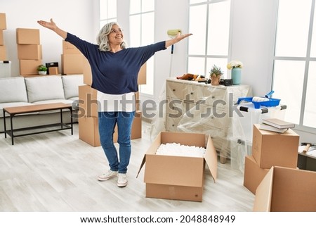Middle age grey-haired woman smiling happy standing with arms opened at new home.