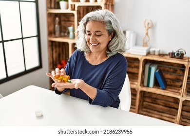 Middle age grey-haired woman taking pills sitting on the table at home. - Shutterstock ID 2186239955