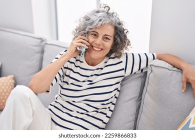 Middle age grey-haired woman talking on the smartphone sitting on sofa at home - Powered by Shutterstock