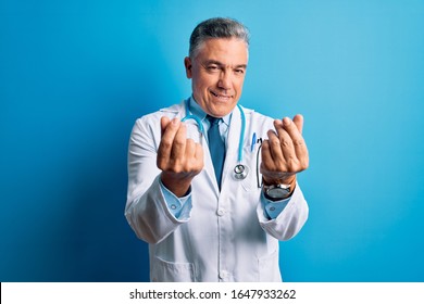 Middle Age Handsome Grey-haired Doctor Man Wearing Coat And Blue Stethoscope Doing Money Gesture With Hands, Asking For Salary Payment, Millionaire Business