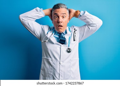 Middle age handsome grey-haired doctor man wearing coat and blue stethoscope Crazy and scared with hands on head, afraid and surprised of shock with open mouth