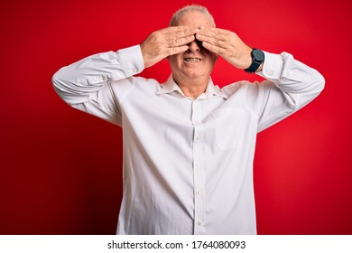 Middle age handsome hoary man wearing casual shirt and glasses over red background covering eyes with hands smiling cheerful and funny. Blind concept. - Powered by Shutterstock