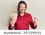 Middle age handsome man holding 100 danish krone banknotes screaming proud, celebrating victory and success very excited with raised arm 