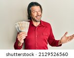 Middle age handsome man holding 100 danish krone banknotes celebrating achievement with happy smile and winner expression with raised hand 
